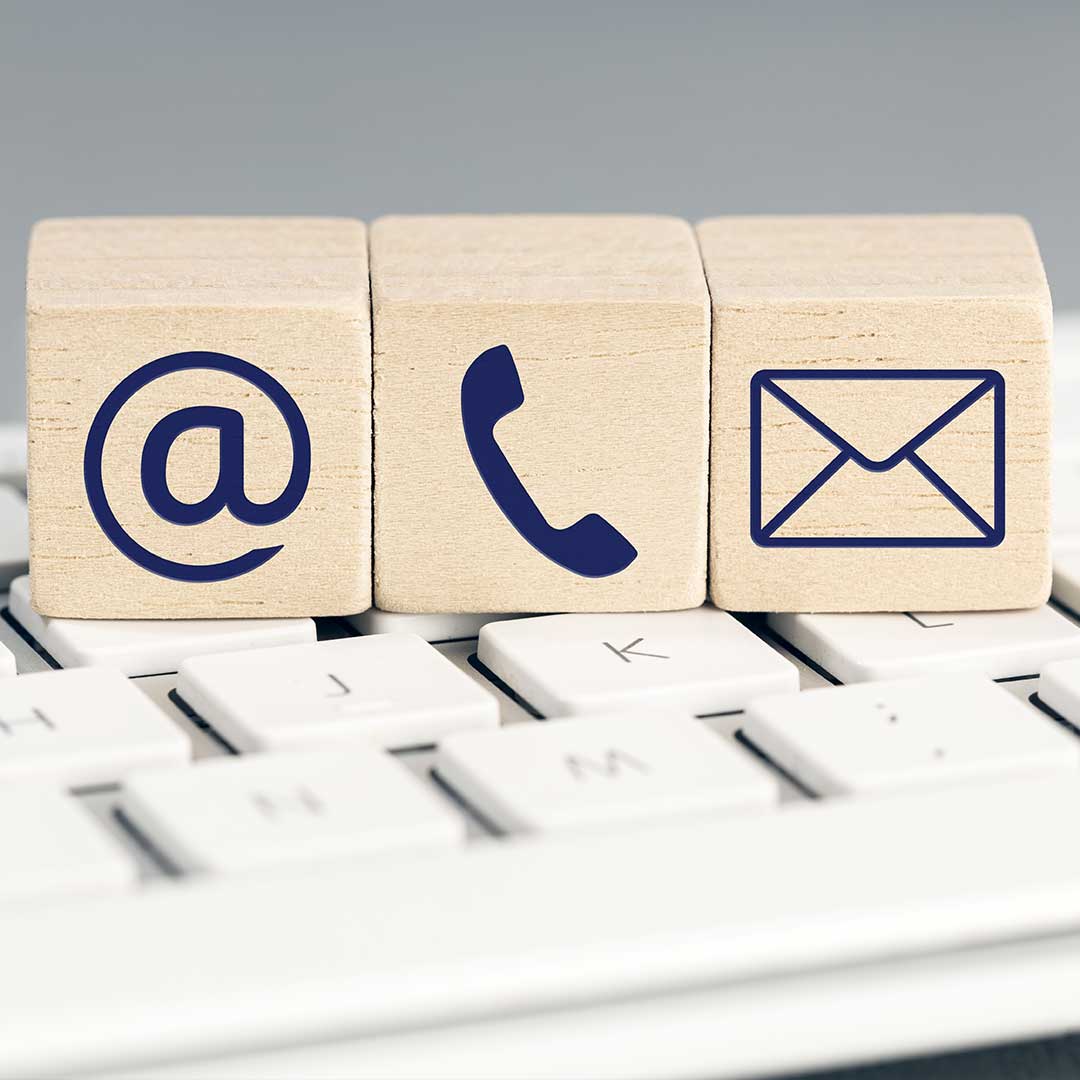 3 small wooden blocks on computer keyboard with icons on each: @, phone, and envelope.